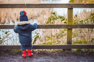 Small child standing behind fence looking over pond 